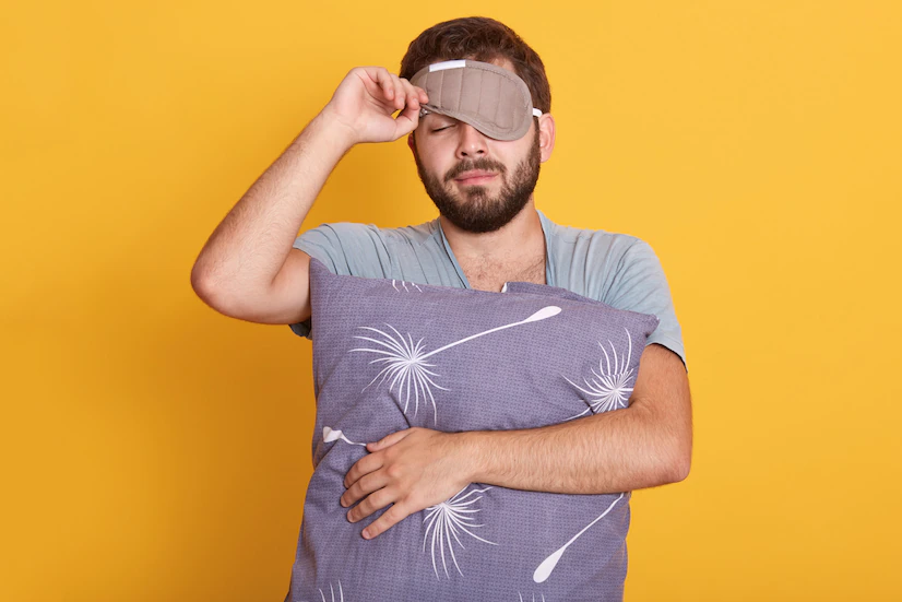 closeup-portrait-sleepy-man-with-blindfold-eyes-holding-pillow-hands-opens-sleeping-mask-keeping-eyes-closed_176532-10269